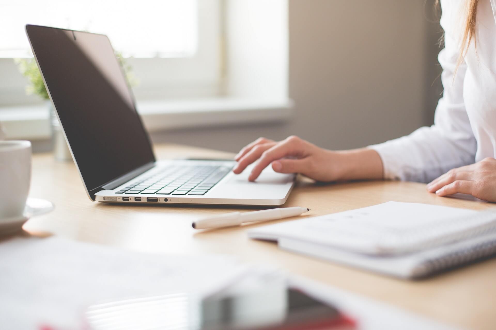 Woman using laptop at desk to look for online chat room software.